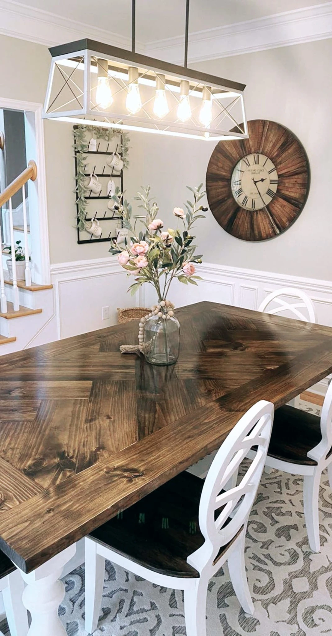 Finished dark-stained herringbone dining table with white chairs and flowers in a bright dining room