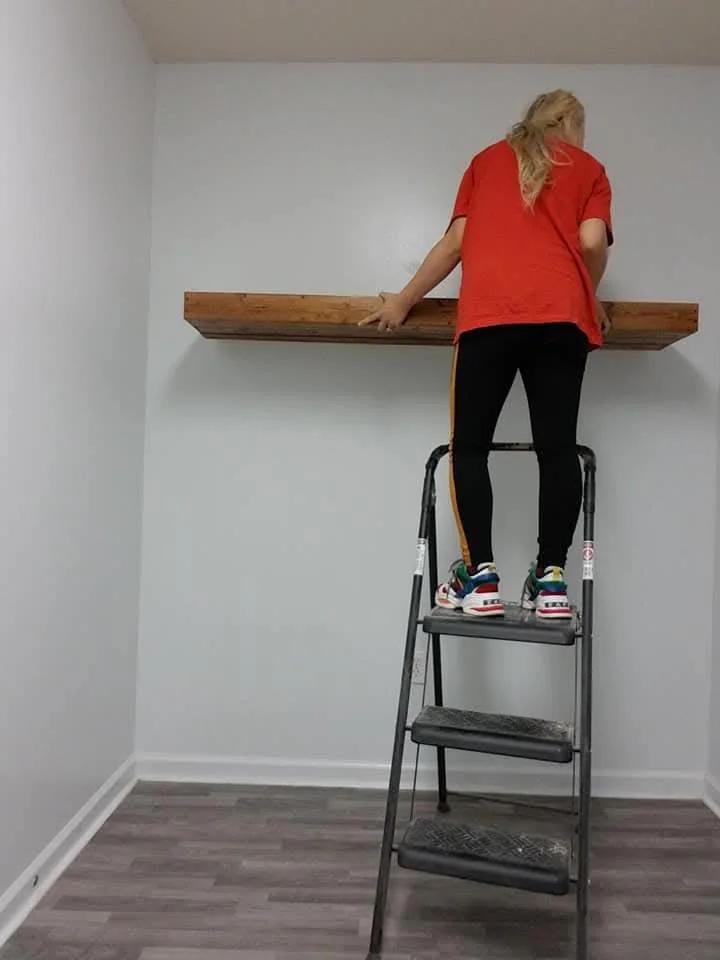 The long wood shelf being placed on the laundry-room wall