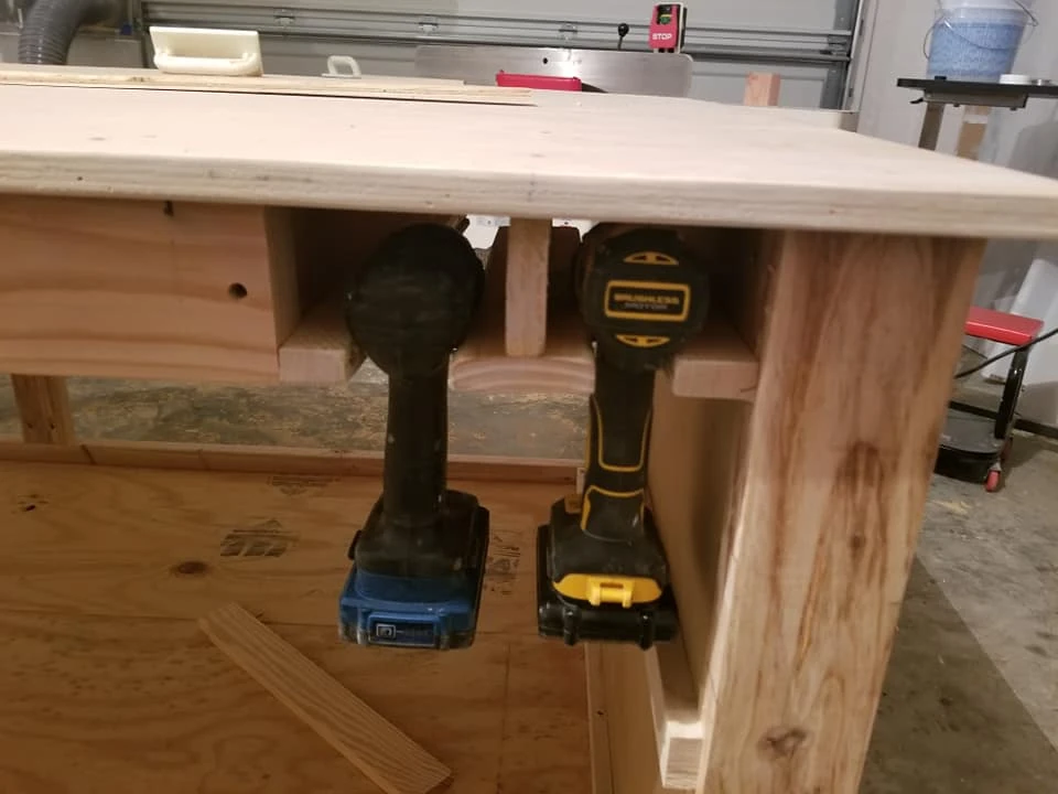 Two cordless drills hanging in wooden holders beneath the bench edge